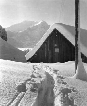 Winterbilder. Hütte im tiefen Schnee. Im Vordergrund Skispuren