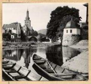 Zwei Ruderboote am Ufer eines Flusses, im Hintergrund mehrere Häuser und ein Kirchturm