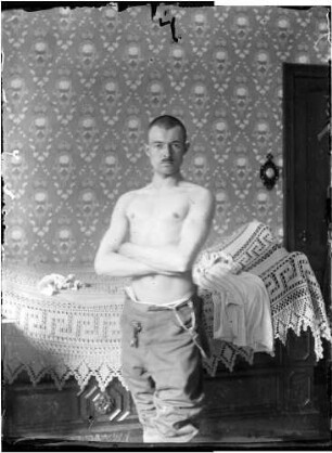 Wolfgang Knochenhauer, stehend mit freiem Oberkörper vor einem Bett posierend