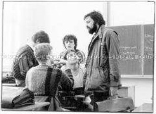 Lehrer im Klassenraum, umringt von Schülern (Altersgruppe 18-21)