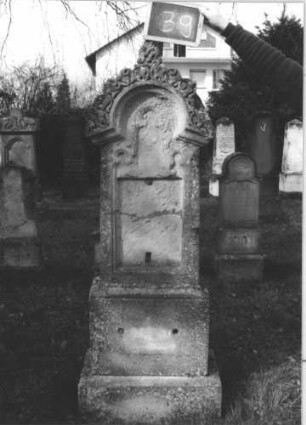 Grabstein 39 (Index: 100112283) Material: Sandstein Zustand: verwittert, Schriftplatten entfernt, zerbrochen und repariert Maße HxBxT: 187x48x21 cm Beschreibung: Stele, getreppter Sockel, eingezogener Rundbogenabschluß mit Mittelakroter, rechteckige Schriftplatten Symbolik: Ranken im Abschluß: Grabstein 39