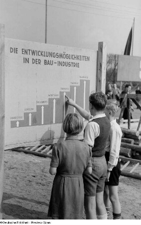Kinder vor einer Informationstafel über die beruflichen Entwicklungsmöglichkeiten in der DDR-Bauindustrie