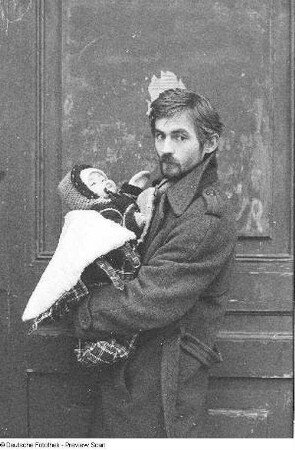 Der Maler Gerd Sonntag vor einer Tür stehend, ein Baby tragend