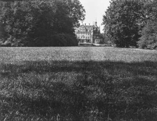 Schloss hinter Bäumen : Blick über eine Wiese auf ein von Bäumen halbverdecktes Schloss