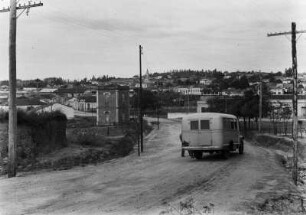 Villa Americana : Blick auf die Häuser von Americana. Im Vordergrund eine unbefestigte Straßen mit einem Fahrzeug darauf. Rechts und links der Straße Masten mit Leitungen.