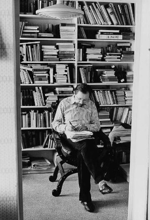 Der Schriftsteller Heinz Czechowski schreibend vor einem Bücherregal sitzend, aufgenommen in seiner Wohnung in Halle-Neustadt