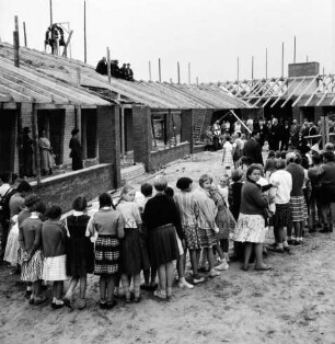 Volksschule: Neubau: Rohbau: Richtfest: vorn Schülerhalbkreis: rechts dahinter Funktionsträger: hinten Pavillonbauten mit Richtkrone und Arbeitern auf Dachsparren