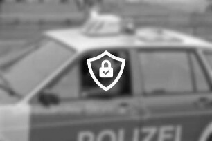 Dorffest: Polizist in Dienstwagen: dahinter Wiese mit Holzzaun und Busch