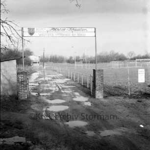 Sporteinrichtungen: Weg am Sportplatz: Sportplatz "Kleines Alster-Stadion" des Wilstedter Sportvereins von 1958 e. V.: vorn Eingangsbereich mit Wasserpfützen auf Weg: rechts Sportplätze: links Holzschuppen: dahinter Sportlerheim: hinten Bäume