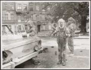 Kinder bemalen in einer Straße ein altes Auto (Altersgruppe bis 14)