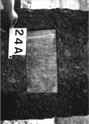 Grabstein 24 (Index: 100081755) Material: Granit, weiße Marmorplatten Zustand: Schriftplatten verwittert mit Textverlus Maße HxBxT: 163x65x34 cm Beschreibung: leicht konische Stele, schräger Abschluß, ovale und querrechteckige Schriftplatten: Grabstein 24A (1)