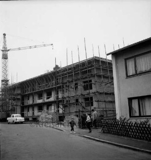 Herrenhusen: Wohnblock: Rohbau mit Gerüst: davor Sandhaufen, Stapel mit Mauersteinen, Pkw: hinten links Baukran: rechts Wohnhaus, Jägerzaun: im Vordergrund Straße: auf Fußweg drei Kinder mit Ball