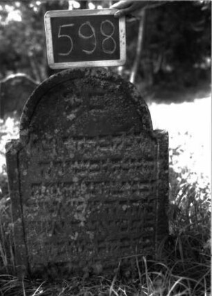 Grabstein 598 (Index: 100102434) Material: Sandstein Zustand: teilweise stark verwittert, eingesunken, teilweiser Textverlust Maße HxBxT: 80x55x9 cm Beschreibung: Stele, eingezogener Rundbogenabschluss, Schriftfeld eingetieft mit Konvexbogenabschluss: Grabstein 598
