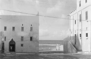 Indische Häuser in Mogadischu : Blick über eine Straße auf zwei Häuser indischen Stils. Zwischen den Häusern ist der Indische Ozean zu erkennen.