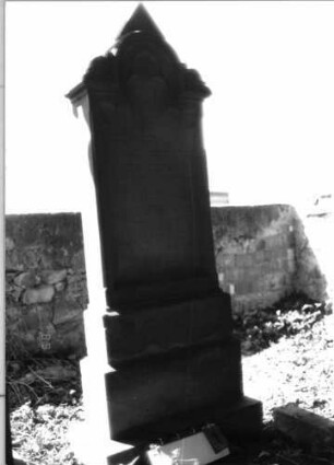Grabstein 1 (Index: 99797996) Material: Sandstein, weiß Zustand: gut Maße HxBxT: 192x62x20 cm Beschreibung: Stele, eingezogener Rundbogenabschluß mit dreieckigem Aufsatz, getreppter Sockel Symbolik: neogotisch, Maßwerk, Dreipaßbogen: Grabstein 1 (1)