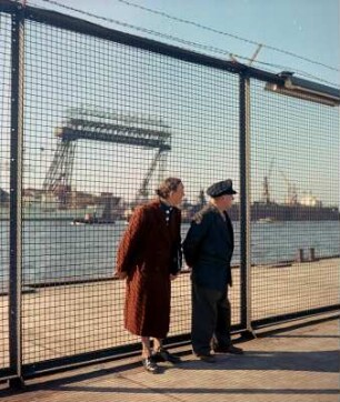 Paar vor einem Drahtgitterzaun von "Blohm + Voss" am Hamburger Hafen