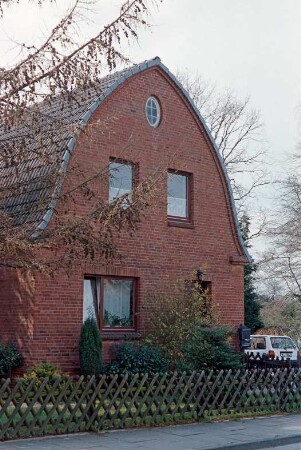 Hasselbusch 25: giebelständiges Wohnhaus aus Backstein mit Spitzbogentonnendach: Straßenfront: vorne Jägerzaun