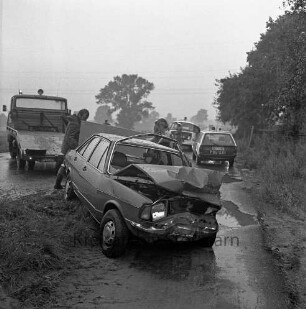 Verkehrsunfall: Landesstraße zwischen Bargteheide und Hammoor: Zusammenstoß von zwei Personenwagen: nasse Fahrbahn: Abschleppwagen, Abtransport eines Pkw mit eingedrücktem Vorderteil, Frau: hinten Einsatzwagen der Polizei, Polizisten: auf Fahrradweg Regenpfützen, 19. August 1980