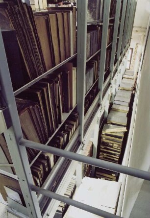 Sächsische Landesbibliothek - Staats- und Universitätsbibliothek Dresden. Zentralbibliothek (ehem. Landesbibliothek). Erdgeschoss (Flachbau). Abteilung Benutzung, Magazin. Blick vom aufgeständerten Zwischenboden nach unten auf gestapelte Bestände : Dresden-Neustadt, Marienallee 12. Sächsische Landesbibliothek - Staats- und Universitätsbibliothek Dresden. Zentralbibliothek (ehem. Landesbibliothek). Erdgeschoss (Flachbau). Abteilung Benutzung, Magazin. Blick vom aufgeständerten Zwischenboden nach unten auf gestapelte Bestände