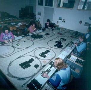 Herstellung von Modelleisenbahn-Fahrzeugen. Mechanikerinnen bei der Montage von Lokomotiven und Güterwagen. Blick auf sechs Arbeitsplätze mit je einer Teststrecke : Herstellung von Modelleisenbahn-Fahrzeugen. Mechanikerinnen bei der Montage von Lokomotiven und Güterwagen. Blick auf sechs Arbeitsplätze mit je einer Teststrecke