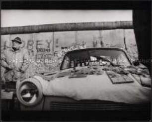 Mann verkauft an der Berliner Mauer auf der Motorhaube seines Trabanten Mauerstücke (Altersgruppe 18-21)