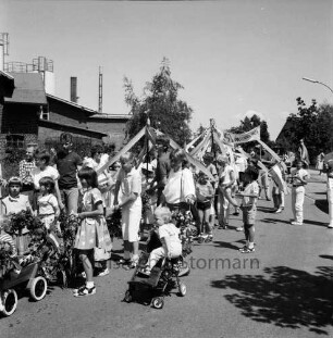 Kindervogelschießen und Dorffest: Festumzug: links Kinder mit Kränzen und geschmückten Bollerwagen und Kinderkarren: rechts Zuschauer: links hinten Gebäude der Paech-Brot GmbH