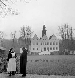 Kloster Nütschau: Herrenhaus: Nordfront mit Außentreppe: davor Rasenfläche: rechts und links Bäume: vorn links Pater Subprior Matthäus Buß und Clemens-Schwester im Gespräch