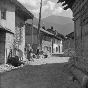 Alltagsbild. Frauen unterwegs in Bansko. Gestelle für das Trocknen der Tabakblätter am Wohnhaus und ein öffentlicher Brunnen in Bansko
