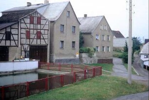 Platz mit eingezäuntem Dorfteich, anliegende Häuser, Wegegabelungen