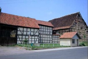 Fachwerkgebäude mit Holztor, Bushaltestelle, stark beschädigter Scheunengiebel