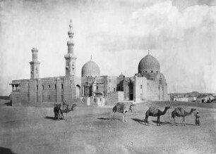 Kairo, Ägypten. Blick auf ruinöse Anlage mit Kuppeln und Minaretten (Mameluckengräber?), im Vordergrund Kamelkarawane mit Einheimischen
