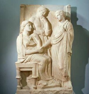 Athen. Archäologisches Nationalmuseum 717. Grabstele mit drei Figuren. Anfang 4. Jh. v. Chr. Links Frau mit Hocker und Fußschemel, Mann mit Himation