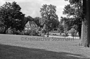 Kurpark: Blick vom Kurparkhügel mit Bäumen auf Rondeel am Sülzberg mit Rabatten und Hecken: hinten links Haus des Handwerks: im Hintergrund Bäume