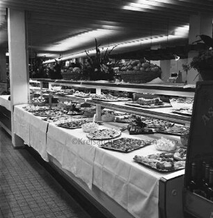 Peters Delikatessen: Mühlenstraße, Ecke Hindenburgstraße: Feinkostgeschäft: 50-jähriges Firmenjubiläum, gleichzeitig Betriebsübergabe: Innenaufnahme: Verkaufsraum: Buffet, Platten und Schüsseln mit Speisen auf Tischtüchern: Blumenschmuck