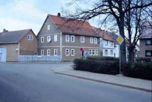 Schulplatz, hinten ehemaliges Schulgebäude; Freifläche mit Hecke und Bäumen