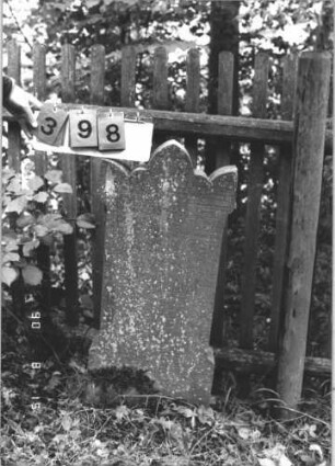 Grabstein 398 (Index: 100106607) Material: Sandstein Zustand: leicht verwittert Maße HxBxT: 99x44x10 cm Beschreibung: Stele mit Volutenabschluß, Mittelpalmette, Schriftfeld rechteckig eingetieft Besonderheit: Kindergrab; - Stele steht mit der Schriftseite am Zaun: Grabstein 398