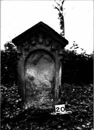 Grabstein 20 (Index: 100106081) Material: Sandstein Zustand: Schrifttafel fehlt oder Schriftfeld völlig verwittert Maße HxBxT: 105x62x21 cm Beschreibung: Stele, giebelartiger Abschluß mit Verdachung, eingetieftes Schriftfeld mit Rundbogen: Grabstein 20