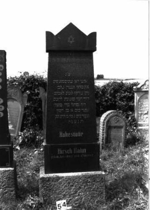 Grabstein 54 (Index: 99891687) Material: schwarzer Basalt Zustand: sehr gut Maße HxBxT: 215x73x13 cm Beschreibung: rechteckige, leicht konisch zulaufende Stele auf Sockel, Giebel als stilisierte Krone (?) Symbolik: Davidstern im Giebel: Grabstein 54