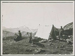 Zwei Personen bei der Rast an einem Zelt mit einer Gebirgslandschaft im Hintergrund