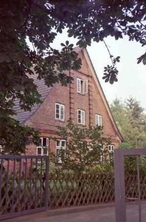 Fritz-Berodt-Straße 6: traufständiges Bauernhaus aus Backstein: Giebelseite Wohntrakt: davor Garten, Jägerzaun: im Vordergrund Einfahrtstor