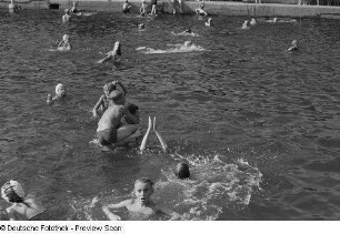 Roger Rössing im Becken des Freibads mit einem Jungen spielend, umgeben von anderen Badegästen