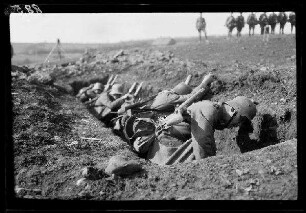 Übungsgelände II bei Mouzon (Dep. Ardennes, Frankreich): Soldaten mit Stahlhelm geduckt in einer Grube, im Hintergrund eine Reihe Offiziere beim Beobachten (Nahaufnahme)