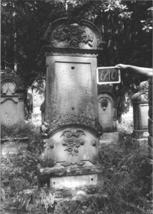 Grabstein 610 (Index: 99895324) Material: Sandstein Zustand: gut; Schriftplatten und Mittelakroter fehlen Maße HxBxT: 202x65x23 cm Beschreibung: Stele mit Aufsatz mit eingezogenem Rundbogenabschluss; Sockel Symbolik: Blumengebinde: Grabstein 610