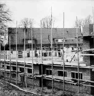Volksschule: Erweiterungsbau für 3. Klasse: Grundmauern mit Gerüsten: darauf Arbeiter: dahinter altes Schulgebäude und Bäume
