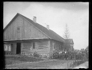 Unbekannte Ortschaft [Litauen/Weißrussland/Ukraine?]: Regimentsmusik neben einem Holzhaus mit Schindeldach (Distanzaufnahme)