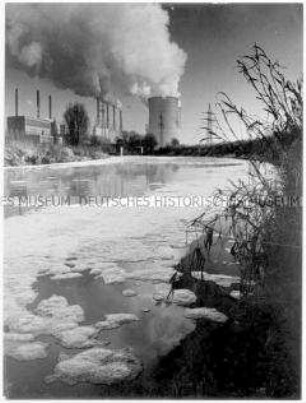 Rauchende Schlote und Kühltürme eines Kraftwerkes und im Vordergrund ein Fluss mit Schaumbildung (Sonderthema: Umweltschutz - Umweltzerstörung)