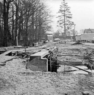 Grönwohldhof: Dorfstraße: Ausbau der Kreisstraße Richtung Dwerkaten: vorn links Brückenbau über die Schönau: hinten Mitte und rechts Baubuden: links Wald: im Hintergrund Häuser