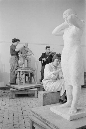 Studenten der Bildhauerklasse von Walter Arnold beim Modellieren. Im Vordergrund die Gips-Statue einerstehenden Frau, ein Kopftuch bindend (1960/1962)