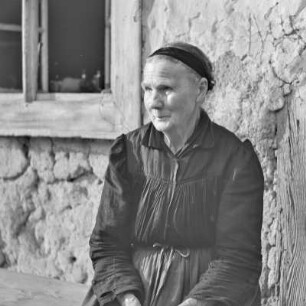 Strohgedecktes Blockhaus in Burg-Kauper. Frau Nowick in Spreewälder Alltagstracht vor ihrem Gehöft. : Ze słomu skryte kładźity twar statoka w Kupaŕskich Bórkowach. Knjeni Nowickowa we wšědnej Błótowskej drasće před swojim statokom.