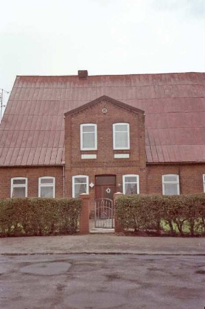traufständiges Bauernhaus aus Backstein: Straßenfront, Teilansicht: Wohntrakt, Eingangsrisalit mit Tür: davor Gartenpforte, Hecke: im Vordergrund Straße